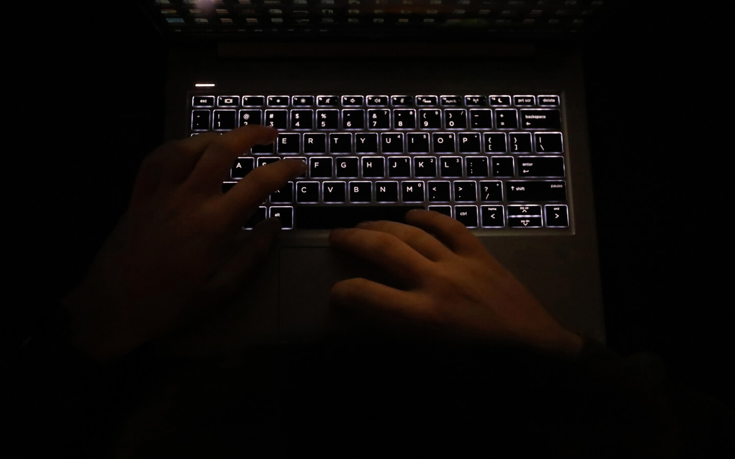 Dark image of hands typing at a computer laptop at night