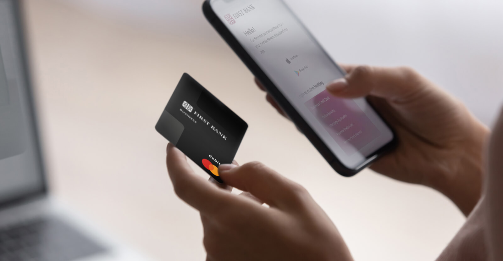 Close up of hands holding First Bank business debit card and cellphone with My First Bank mobile banking app.
